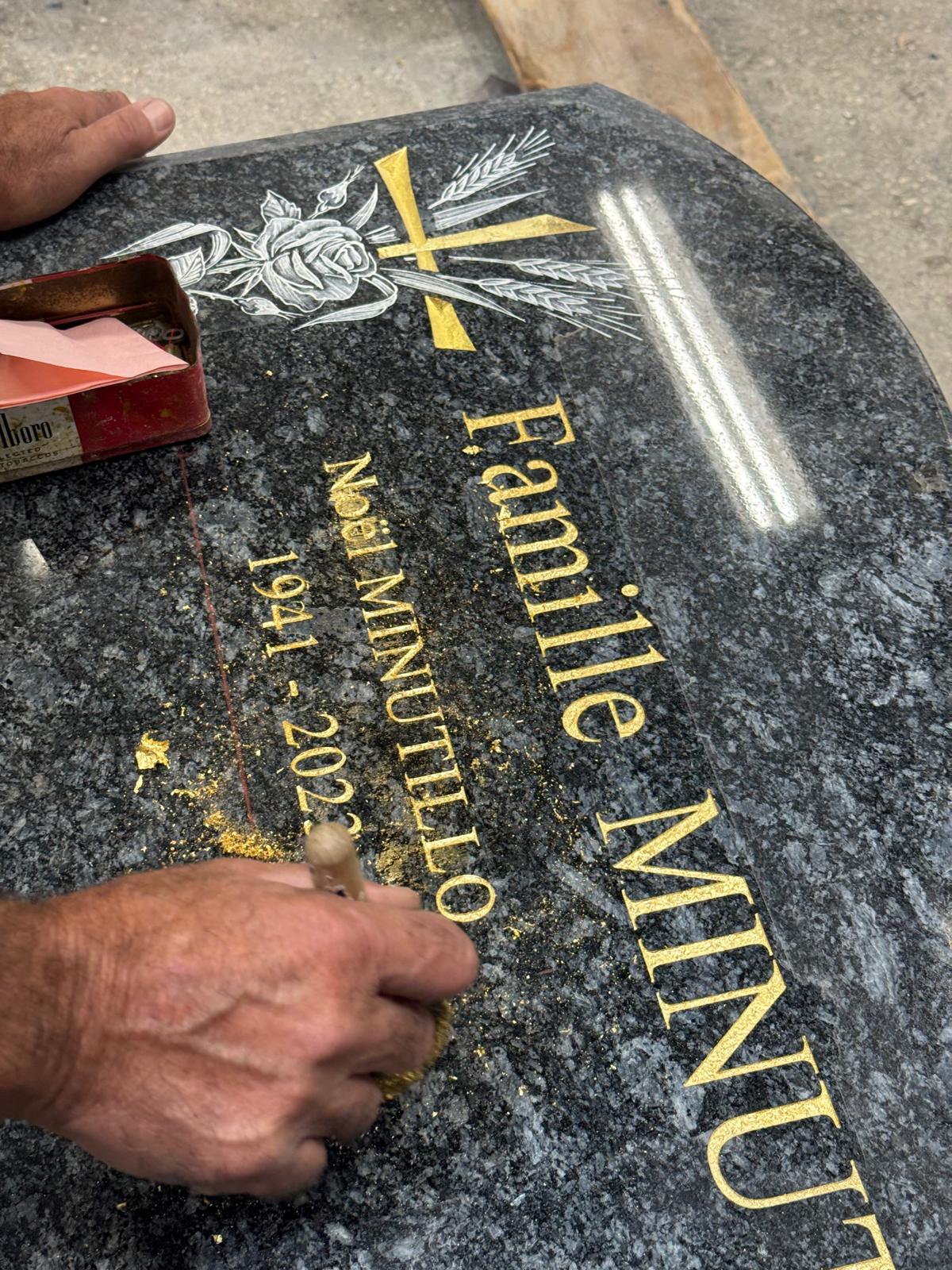 Gravure et dorure à la feuille d'or d'une stèle en granit, savoir-faire artisanal