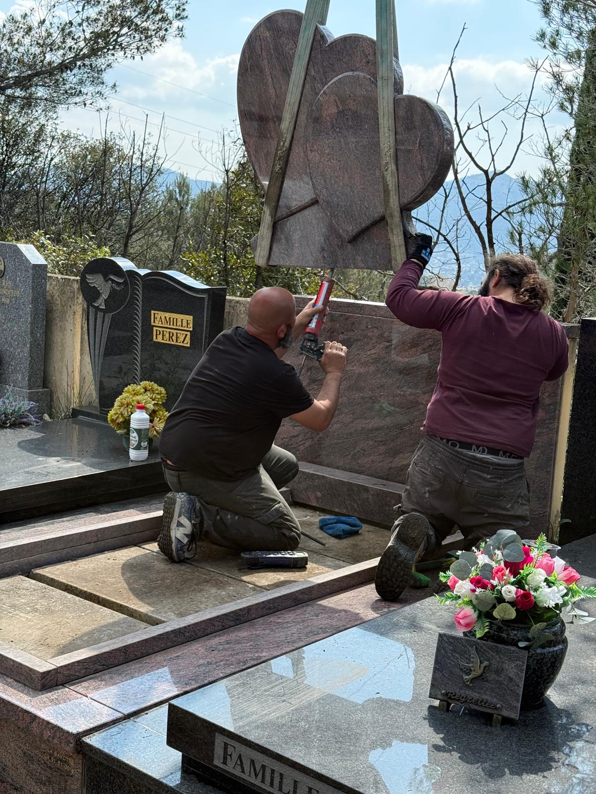 Deux marbriers posant un monument funéraire en granit à double cœur dans un cimetière