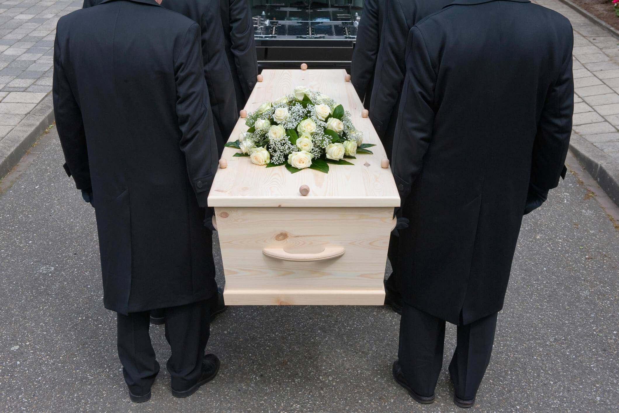 Des porteurs en habit sombre portant un cercueil clair fleuri de roses blanches, avec dignité